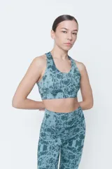 Top deportivo de lycra color verde con estampado abstracto en tonos verde oscuro y celeste. Espalda cruzada y compresión alta.
