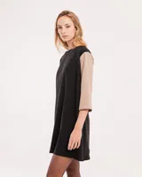 Vestido corto negro con mangas 3/4 verdes, cuello bote y bolsillos laterales.