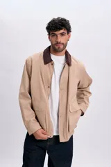 Campera color taupe con cuello de pana marrón oscuro, cierre frontal y botones a presión. Cuenta con dos bolsillos frontales con solapa.