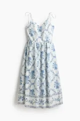 Vestido midi de popelina de algodón en color blanco con estampado floral azul, escote corazón y tirantes finos de lazo. Presenta cuerpo entallado, espalda elástica tipo nido de abeja y falda amplia con vuelo.