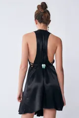 Vestido midi negro de tejido sastrero fino y liso con leve brillo. Tiene escote en V, tiras para ajustar en la cintura, volado asimétrico en el ruedo y espalda descubierta.