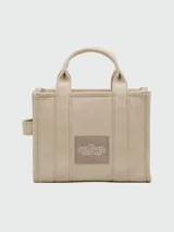 Bolso tipo tote de Marc Jacobs, confeccionado en lona resistente color beige. Presenta el logo estampado en contraste en el frente, doble asa superior y cierre superior con cremallera.
