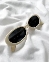 Lentes de sol con montura ovalada color crema y cristales negros.