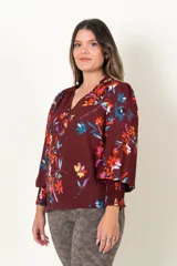 Blusa color borgoña con estampado de flores multicolores, escote en V con botones forrados, mangas largas con frunces en los puños y hombros.