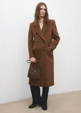 Bolso de mano tipo bandolera confeccionado en piel bovina de color marrón. Cuenta con un diseño estructurado, solapa frontal con detalle de trabilla y hebilla metálica, y asa corta para llevar al hombro o en la mano.
