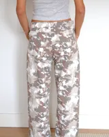 Pantalon de corte recto con estampado camuflado en tonos neutros, beige y marron. Presenta costuras verticales frontales que recorren el largo de las piernas, bolsillos laterales y cierre frontal con boton.