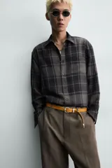 Camisa de corte relajado confeccionada en tejido fluido con mezcla de viscosa. Presenta diseño de cuadros en tonos grises y azul oscuro, cuello solapa, manga larga con puños abotonados y cierre frontal de botones.