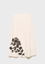Falda midi de tiro alto con corte evasé, confeccionada en una mezcla de algodón y lino color beige. Presenta un diseño bordado floral en color negro ubicado en el lateral inferior.