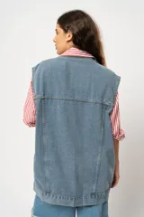 Chaleco oversize de jean celeste con cuello clásico, cierre frontal con botones metálicos, dos bolsillos con solapa en el pecho y corte a la cadera. Sin mangas.