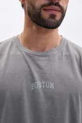 Remera de manga corta color gris oscuro con efecto lavado, corte holgado y estampado arqueado en la espalda con los nombres de ciudades: "New York", "Amsterdam" y "Boston".