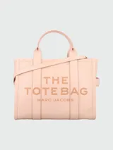 Bolso tipo tote mediano de cuero, color rosa pálido, con asas superiores y correa cruzada ajustable y desmontable. Presenta el logo estampado en el frente con el texto "THE TOTE BAG MARC JACOBS".