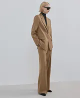 Pantalón de vestir tostado de tiro medio, con pernera ancha y recta, bolsillos laterales y pliegue planchado central.