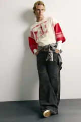 Jeans flare fit de denim de algodón negro con efecto desgastado, roturas, costuras decorativas en las perneras y bajo irregular deshilachado.