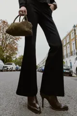 Pantalón flare de tiro bajo color marrón oscuro, con bolsillos delanteros y traseros, pierna entallada y bajo acampanado. Cierre frontal con cremallera y botón.