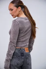 Remera de manga larga color gris con efecto acid wash, cuello redondo y detalles de pedrería plateada alrededor del cuello. Las mangas tienen un diseño que cubre parcialmente las manos.