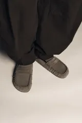 Zueco destalonado tipo mocasín confeccionado en piel, con interior forrado en pelo sintético. Presenta antifaz en el empeine, costuras decorativas y punta redonda.