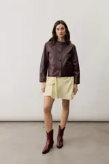 Chaqueta de cuero negra con cuello redondo, cierre frontal de botones forrados y bolsillos ribeteados con detalles de costura decorativa.