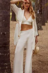 Conjunto de tres piezas en color blanco, compuesto por una camisa de manga larga con ajuste en la cintura, un top corto tipo bralette y un pantalón de corte recto y holgado.