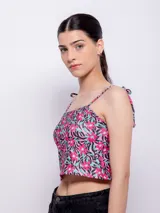 Top corto con escote recto y tirantes finos ajustables mediante nudo en los hombros. Presenta un estampado floral sobre fondo oscuro, con flores rosadas y hojas turquesas.