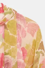 Vestido midi con estampado floral en tonos rosados, verdes y ocres. Presenta cuello con lazo, escote en pico, mangas largas con puños y cintura elástica con cinturón ajustable del mismo tejido. La falda cuenta con un diseño plisado y forro interior.