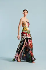 Vestido largo strapless de diseño entallado, con estampado floral multicolor sobre base negra, falda con abertura frontal pronunciada y superposición de capas.