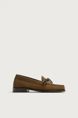 Mocasín de vestir para hombre confeccionado en piel con acabado en gamuza de color marrón, con punta redonda, suela oscura con ligero tacón y detalle de lazo en el empeine.