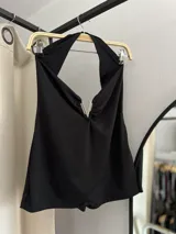 Catsuit corto negro, ajustado al cuerpo, con escote pronunciado en V y detalle de cierre metálico en forma de V en el centro del busto.