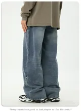 Pantalón de jean de corte relajado y ancho, color azul medio desgastado, con costuras decorativas en diagonal en la parte delantera de las piernas y bolsillos traseros.