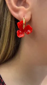Caravanas de argolla dorada con dije colgante en forma de flor de tres pétalos de color rojo brillante.
