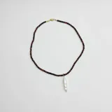 Collar compuesto por pequeñas cuentas de piedra Ojo de Buey y un dije central de perla de río natural, con cierre y detalles en baño de oro.