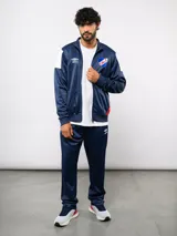 Conjunto deportivo Umbro del Club Nacional de Football, compuesto por una campera con cierre frontal y un pantalón a juego. Ambas piezas son de color azul marino con detalles en blanco y rojo, presentando el escudo del club y el logo de la marca.