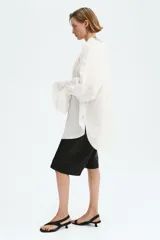 Camisa de lino y viscosa color blanco marfil, de diseño oversized, con cuello alto plisado y volados, mangas largas abullonadas con puños elásticos fruncidos y cordones ajustables en el escote.
