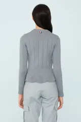 Sweater gris de punto con calce al cuerpo, volado en el ruedo y botones decorativos en el hombro.