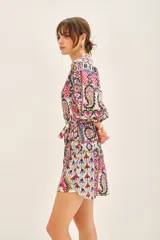 Vestido corto de cuello redondo con escote en V, mangas 3/4 con puños elásticos y lazo ajustable en la cintura. Presenta un estampado multicolor con motivos geométricos y florales.