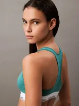 Bralette deportivo sin forro ni relleno, color verde azulado, con espalda cruzada y banda elástica inferior con logo de Calvin Klein repetido.