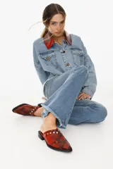 Mules de cuero color rojo con estampado de serpiente y detalles de tachas plateadas en el empeine. Tienen punta en pico y tacón bajo.