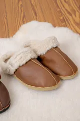 Pantufla de cuero color habano con interior y borde de lana de oveja, suela plana de goma.