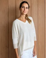 Sweater de punto en color crudo, con cuello en V, mangas tres cuartos y diseño holgado. Presenta detalles de ribetes en tono beige en los puños y en el ruedo.