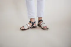 Sandalias de cuero color blanco y plateado, con tiras anchas y ajuste con hebilla. Suela track color caramelo.