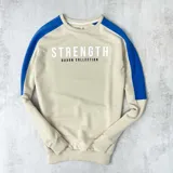 Buzo color arena con mangas ranglan azul eléctrico y estampa frontal con la palabra "Strength" y la frase "Duxon Collection".