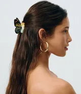 Pinza para el pelo con diseño de mariposa, fabricada en acrílico con detalles coloridos en tonos amarillos, verdes y negros en las alas.