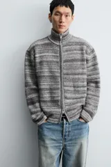 Chaqueta de punto con diseño de rayas horizontales en tonos grises, cuello subido y cierre frontal de cremallera completa. Presenta un corte relajado y acabados en rib en puños y bajo.