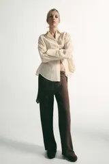 Pantalón de tiro medio con pernera recta y amplia, confeccionado en tejido con textura. Presenta una pieza superpuesta tipo pañuelo anudada en la cintura y bajo ajustable con botón.