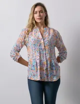 Blusa de gasa estampada con flores en tonos rosa, amarillo y azul. Tiene cuello a la base, escote en V y botones. La delantera tiene detalle plisado y las mangas son 3/4 regulables con presilla y botón.