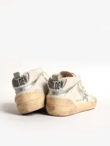 Zapatillas urbanas de caña media, color blanco hueso, con detalles desgastados. Presentan una estrella de glitter plateado en el lateral, cordones blancos y suela de goma color caramelo.