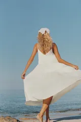 Vestido largo satinado color crudo, con escote en pico adornado con lazada y tirantes finos ajustables. Presenta detalles de frunces y diseño fluido.