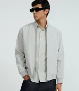 Campera bomber gris claro de poliéster con revestimiento de poliuretano, cuello, puños y ruedo de rib elástico, con cierre frontal de cremallera y tecnología repelente al agua.