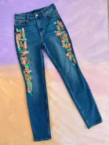 Jean de denim azul de corte ajustado, con diseño pintado a mano en la parte delantera simulando pinceladas abstractas en tonos rosado, celeste y marrón.