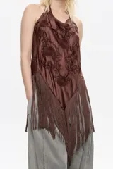 Top de corte fluido color marrón oscuro, con escote halter ajustable mediante cintas anudadas en el cuello. Presenta bordados florales tonales en el frente y un bajo con flecos largos en forma de pico.