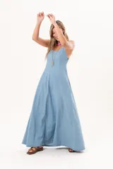 Vestido largo de denim fino y liviano, color celeste, con breteles finos, escote delicado, silueta entallada en la parte superior, falda amplia con recortes verticales y bolsillos laterales.